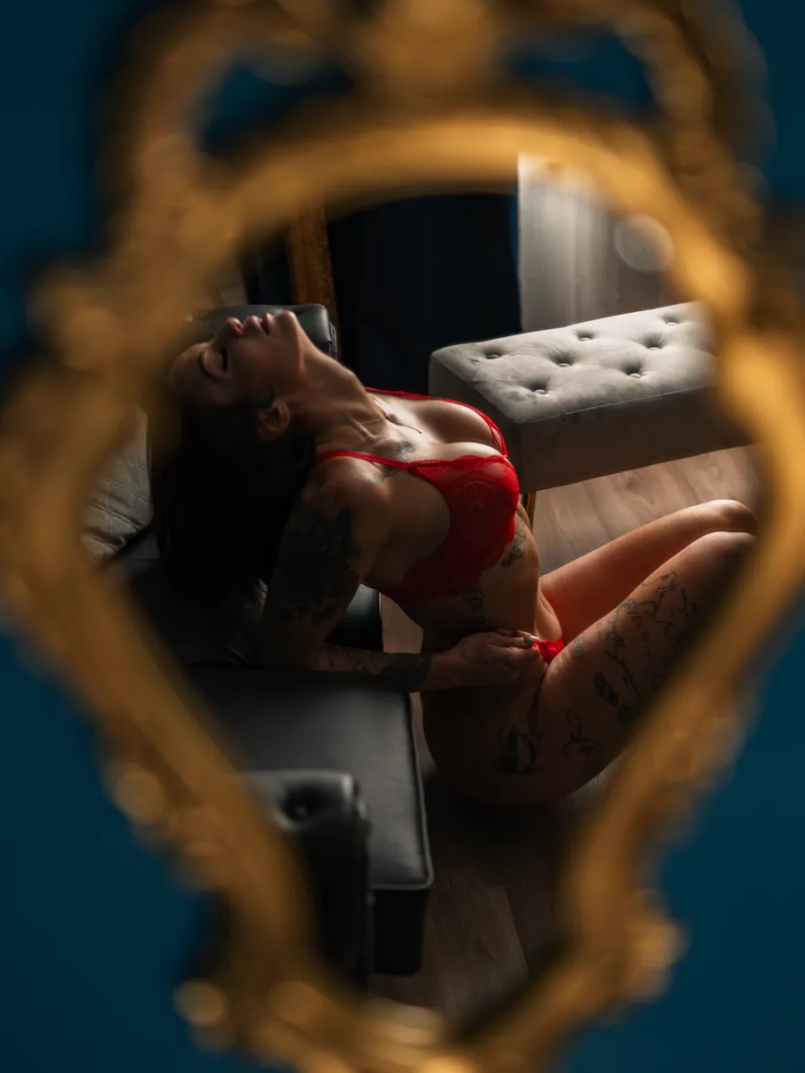 Cyane Reyes en lingerie rouge, vue à travers un miroir doré.