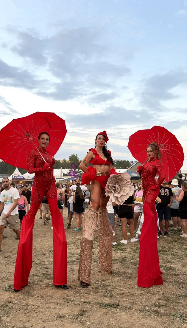 Trois échassières en rouge avec ombrelles, en plein air.