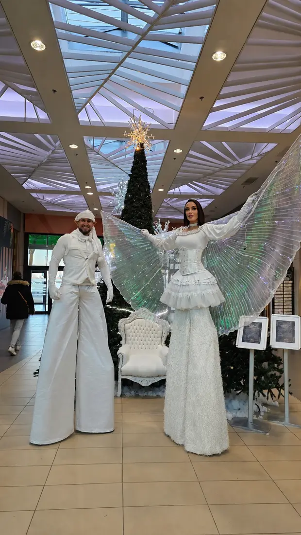 Deux échassiers en blanc, ailes lumineuses déployées, dans une salle de réception.