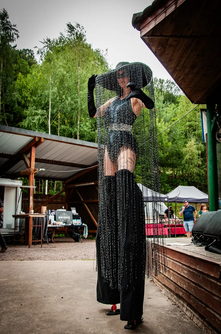 Échassière en robe noire et chapeau à larges bords, voilette en résille.