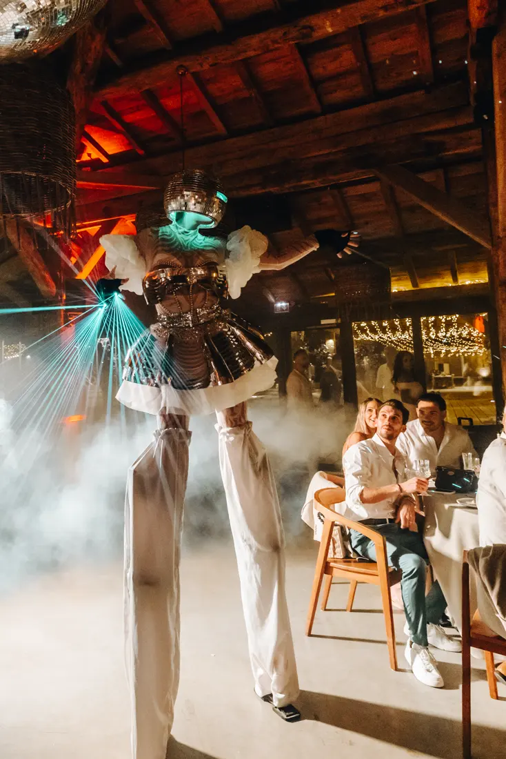 Échassière à tête de boule à facettes, entre lasers et fumée, au milieu des invités d'une soirée.