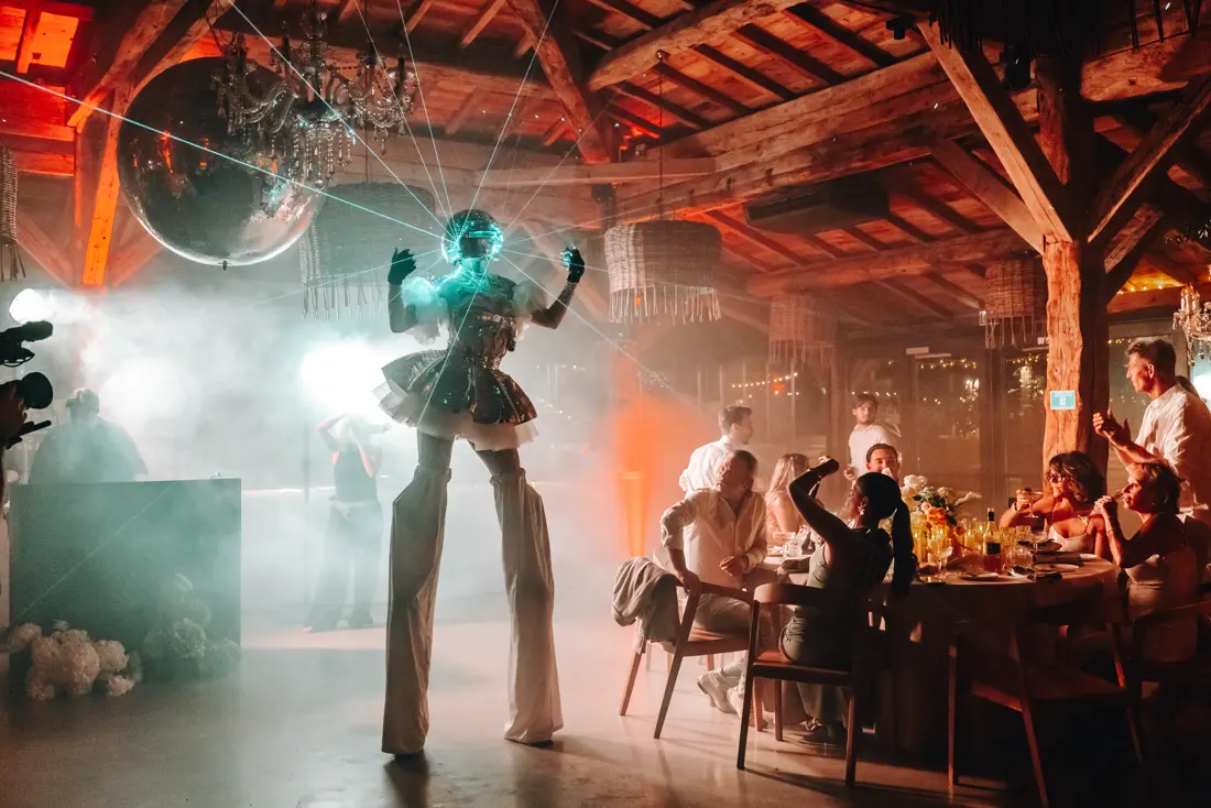 Échassière à tête miroir sous une boule à facettes, rayons laser au-dessus des tables d'un dîner.